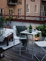 Patio exterior moderno con mesa e cadeiras brancas FEJAN, mantas, viño, plantas e velas, creando un ambiente acolledor da noite.