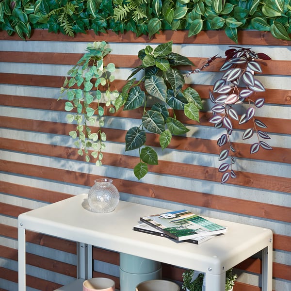 As plantas falsas montadas na parede decoran un valado de madeira. Unha mesa branca contén un vaso e revistas.
