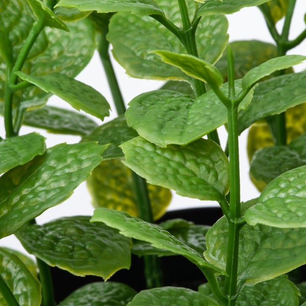 Primeiro plano de follas verdes vibrantes e realistas dunha planta artificial en pota.