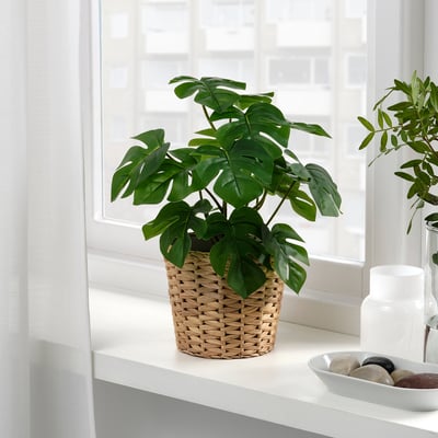 Unha planta falsa en pota está sentada xunto a unha fiestra, levando a natureza ao interior sen necesidade de coidados.