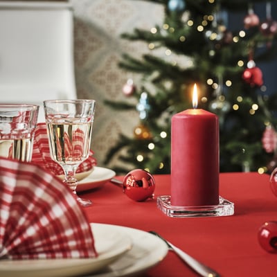 Vela vermella en soporte de vidro na mesa festiva con pratos e vasos, creando calor e acollemento.