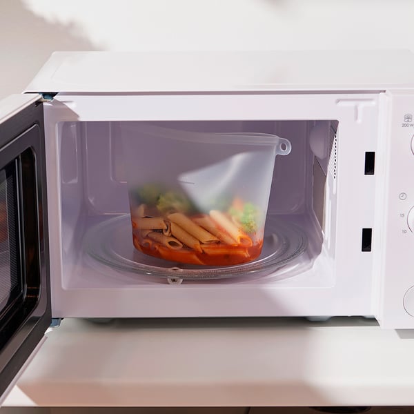 Unha bolsa de plástico transparente con pasta e verduras dentro dun microondas, lista para quentar de novo.