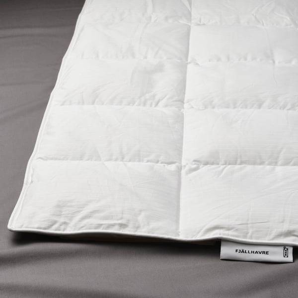 Primeiro plano de duvet branco de fjällräven na cama con patrín cosido en caixa e etiqueta FJÄLLHAVRE.
