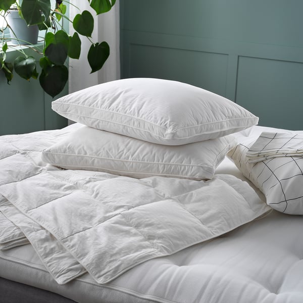 Un duvet FJÄLLHAVRE branco e fluffy cun patrán de punto de caixa nunha cama. O duvet está rodeado de almofadas brancas e un aspecto suave e invitante.
