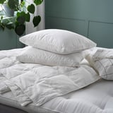 Un duvet FJÄLLHAVRE branco e fluffy cun patrán de punto de caixa nunha cama. O duvet está rodeado de almofadas brancas e un aspecto suave e invitante.