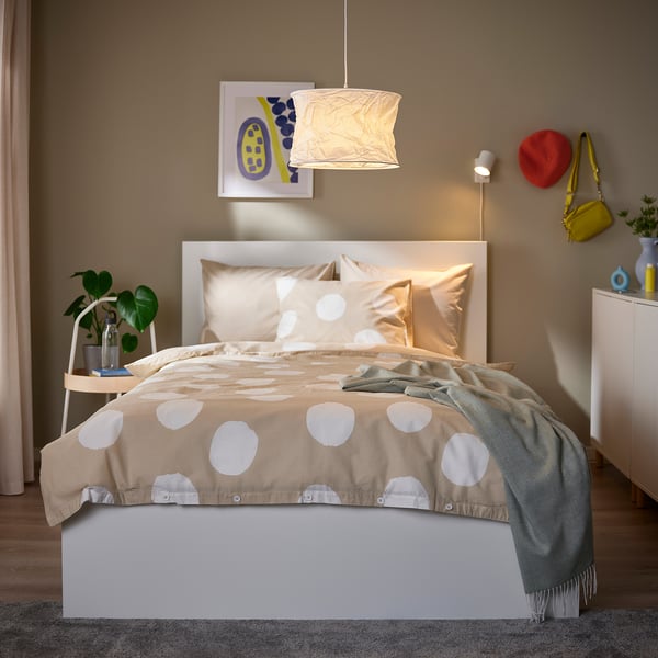 Dormitorio acolledor con lámpada FJÄLLMIL branca, cama elegante, manta verde e planta.