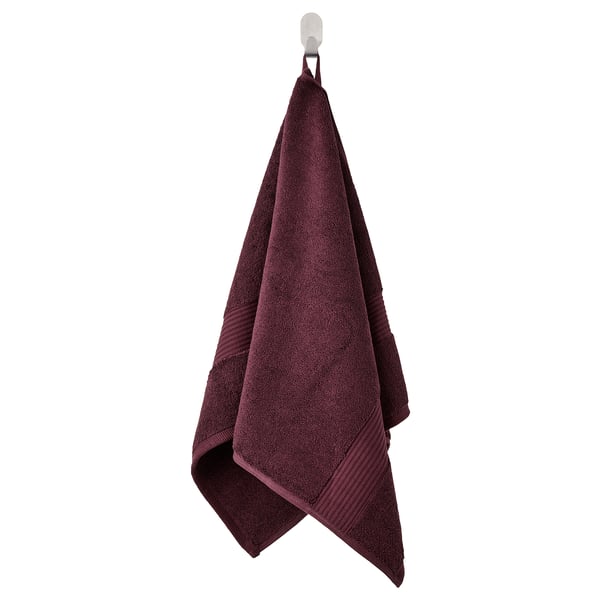 A toalla de baño de Fredriksjon púrpura escura colga ordenadamente, feita de algodón 100%, dobrada cun bordo decorativo bordado.