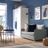 Moderno sofá azul en habitación acolledora. Situado entre o armario alto e a arte da parede. Máis pequeno que o armario, máis grande que a mesa lateral.