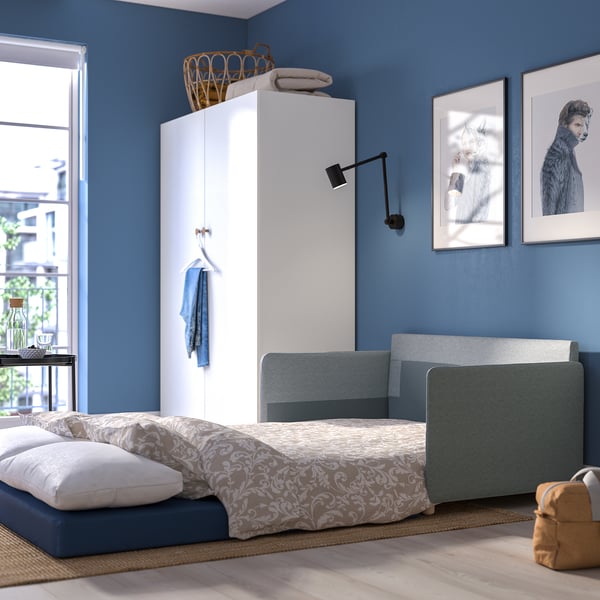 Sofá cama moderno e compacto nunha habitación pequena. Parede azul, armario branco, arte do gato. Fácil de converter para durmir.