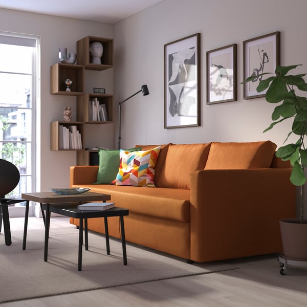 Unha acolledora sala de estar cun sofá laranxa brillante FRIHETEN, unha moderna mesa de café e un estante de libros cheo de libros.