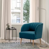 Cadeira de barril verde azul con patas de madeira xunto á fiestra.
