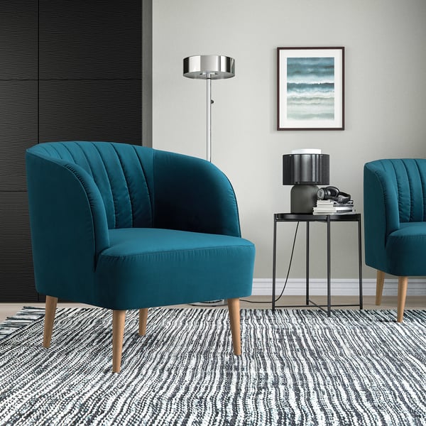 Sala de estar moderna con cadeiras de barril FULLÖSA verde azul, mesa lateral negra delgada, alfombra con patróns, lámpada de chan prateada e arte de parede.