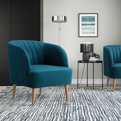 Sala de estar moderna con cadeiras de barril FULLÖSA verde azul, mesa lateral negra delgada, alfombra con patróns, lámpada de chan prateada e arte de parede.