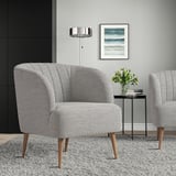 Cadeira de barril gris moderna FULLÖSA, pequena e elegante, patas de madeira; Colocado preto da mesa lateral de metal negro con flores. Obra de arte e lámpada na parede.