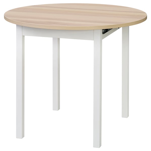 Representa unha mesa de comedor de madeira redonda e extensible con patas brancas. Está deseñado para 2-4 persoas e ten unha parte superior lisa, de cor clara.