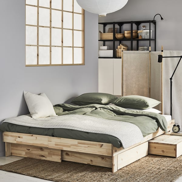 Dormitorio minimalista con cama de piñeiro GLAMBERGET, roupa verde, almofadas brancas e estantes de parede.