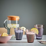 Tres vasos púrpura con franxas de limón sentan xunto a unha xerra con xeo e auga.