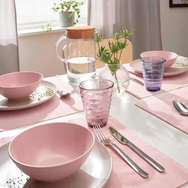 Unha mesa con cuncas rosas coloridas, vasos remuíños e cubertas metálicas, acentuadas por un vaso de vidro texturizado con flores.