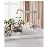 Nova billa cromada GLITTRAN sobre lavabo de mármore branco, con vaso claro de flores frescas preto.