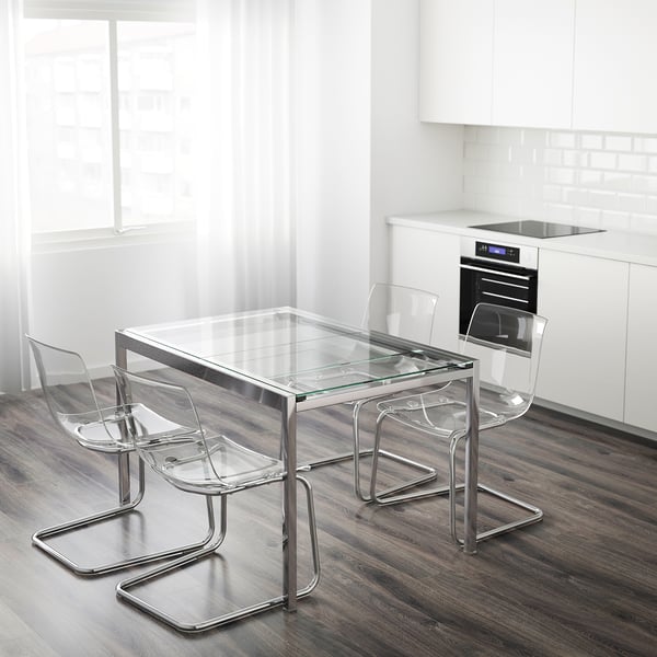 Conxunto de comedor moderno con cadeiras transparentes e mesa de vidro. A mesa de vidro esténdese para hóspedes adicionais. Cadeiras apilables. Fondo branco de cociña.