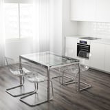 Conxunto de comedor moderno con cadeiras transparentes e mesa de vidro. A mesa de vidro esténdese para hóspedes adicionais. Cadeiras apilables. Fondo branco de cociña.