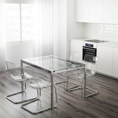Conxunto de comedor moderno con cadeiras transparentes e mesa de vidro. A mesa de vidro esténdese para hóspedes adicionais. Cadeiras apilables. Fondo branco de cociña.