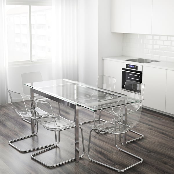 Cociña moderna con mesa de vidro GLIVARP e cadeiras transparentes. Rectangular, esténdese para 4-6, marco cromato. Cortinas e armarios brancos, forno visible.