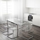 Cociña moderna con mesa de vidro GLIVARP e cadeiras transparentes. Rectangular, esténdese para 4-6, marco cromato. Cortinas e armarios brancos, forno visible.