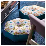Coxíns amarelos GOKVÄLLÅ con lados azul nunha alfombra azul, perna da cadeira visible.