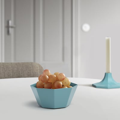 Unha pequena cunca hexagonal azul contén uvas. Nun ambiente minimalista, a cunca aséntase nunha mesa branca preto dun portavelas turquesa.