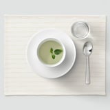 Cunca branca con sopa verde, basilico, culler, cunca sobre alfombra.