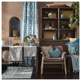 Sala de estar de luxo con decoración azul e beige. Cortinas con patróns, almofadas e alfombras, xunto con mobles e plantas de madeira.