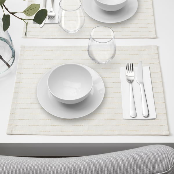 Mesa con 4 alfombras GOKVÄLLÅ de cor crema, cada unha con pratos brancos, vasos e pratería. As alfombras son menos anchas que os pratos que conteñen.
