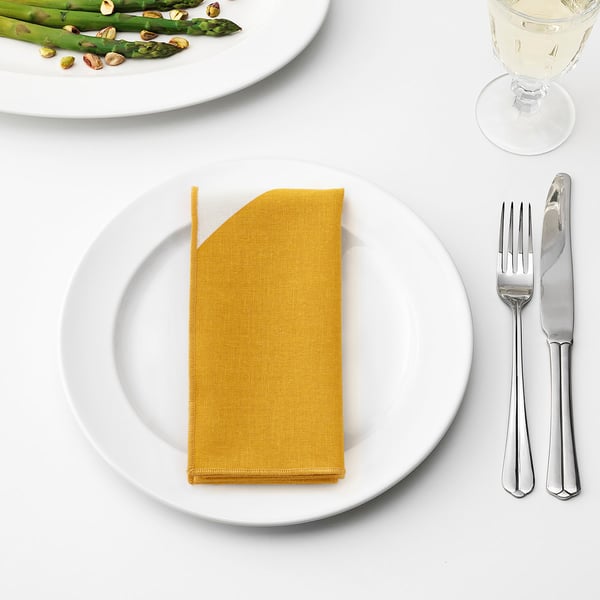 Mesa con servilleta amarela, garfo, coitelo, prato de espárragos e vaso de viño.