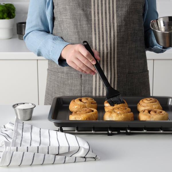 Unha persoa está a cepillalo de produtos de forno cun cepillo de silicona. A bandexa e os ingredientes están enriba da mesa.
