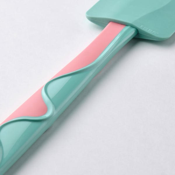 Espátula de silicona turquesa e rosa sobre superficie branca. Lámina suave e flexíbel para raspar eficientemente.