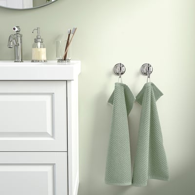 Baño moderno con vanidade branca, cromo, 2 toallas verdes e pequena decoración.