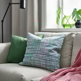 Almofada decorativa HAMNKRASSING con raias no sofá, máis pequena, lámpada verde, planta detrás.