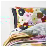 Almofada floral multicolor brillante con base verde a cadros sobre fondo branco.