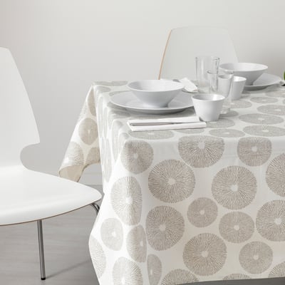 Unha mesa de comedor branca con pano de mesa circular gris, rodeada de cadeiras brancas, con pratos, cuncas e vasos.