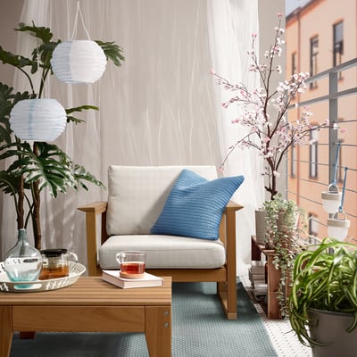 Patio acolledor con cadeira de brazos beige HATTHOLMEN, coxín azul, té e plantas.