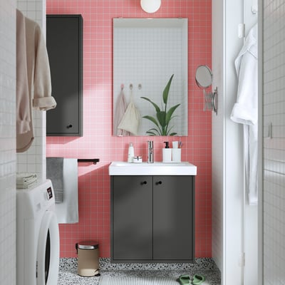 Pequeno baño moderno con baldosas rosas, armario gris escuro, lavabo branco, espello e lavadora, cun deseño sinxelo.