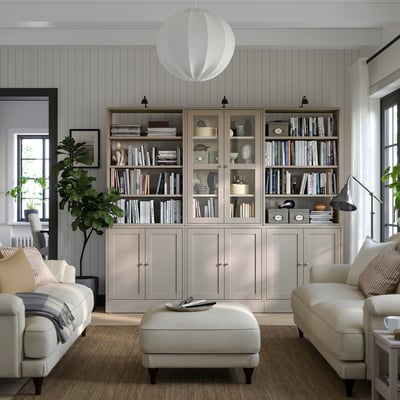 Sala de estar moderna con librarías de piñeiro gris claro HAVSTA cheas de libros, sofá branco e paredes grises e lámpadas colgantes.