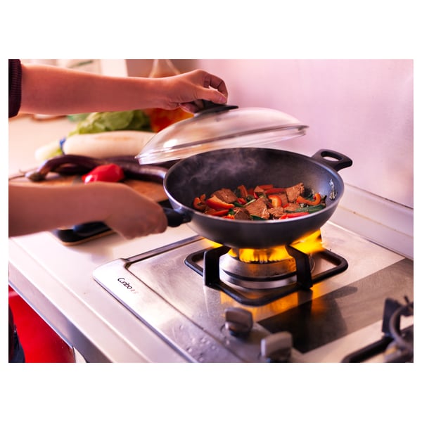 Levanta a man a tapa do wok na estufa, mostrando comida frita con vapor subindo, indicando a cocción activa.