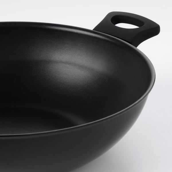 Wok negro con revestimento antiadherente e mangos robustos sobre superficie branca.
