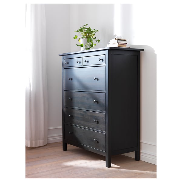 Cofre HEMNES de madeira negra con cinco caixóns, rematado cunha planta e libros.