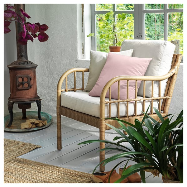 Unha cadeira de brazos de vimbio HOLMSTA con coxíns beige e rosa. É materiais naturais como ratán e bambú, creando un deseño acolledor e rústico.