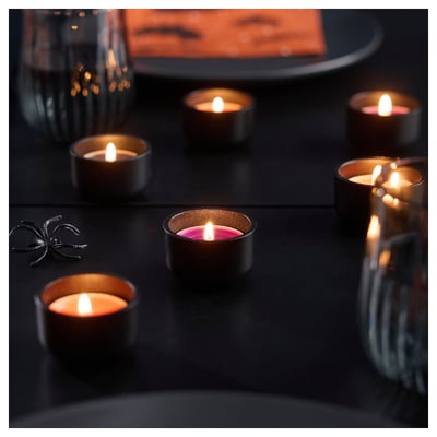 Seis luces de té acendidas nunha superficie escura, creando un brillo cálido e acolledor. Unha luz de té emite un ton rosa suave. O seu agradable cheiro a vainilla enche o cuarto.