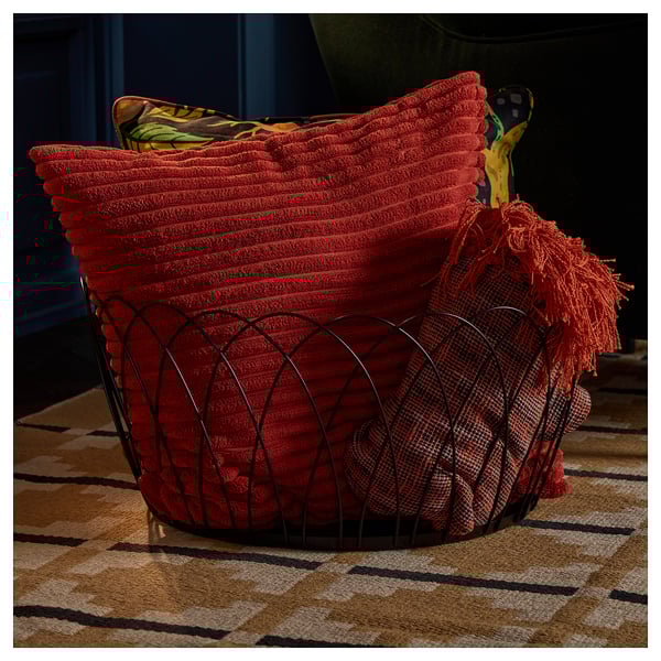 Cesta de arame decorativa con mantas vermellas, ideal para almacenar obxectos grandes preto do sofá ou da cheminea.