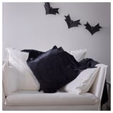 Sofá branco con almofadas negras en forma de morcego, unha con cremalleira, para a decoración de Halloween.